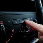 Close-up of a person adjusting a car's air conditioning system inside a vehicle cabin.