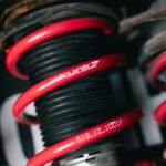 Detailed view of a red coilover suspension spring with visible branding. Automotive part.